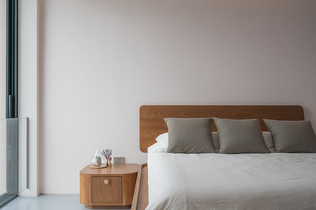 A minimal, modern bedroom with a wooden headboard, nightstand, and neutral bedding.