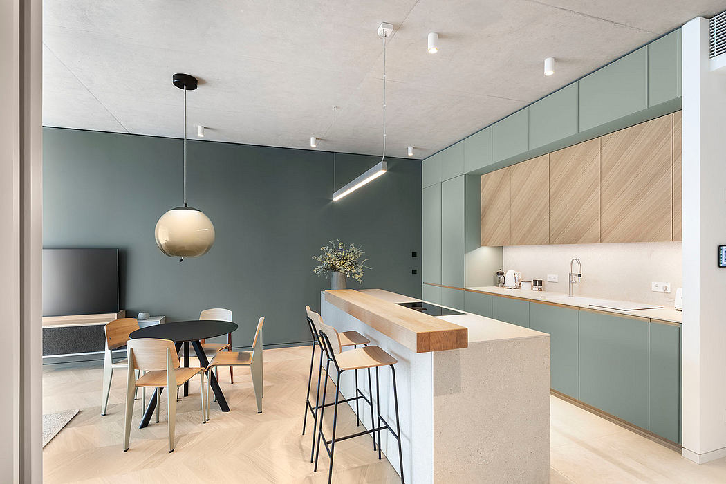 Sleek, minimalist kitchen with sage green cabinetry, wooden countertop, and pendant lighting.