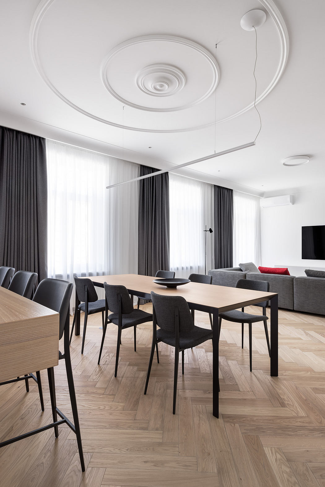 A modern dining room with a spiral ceiling design, sleek furniture, and parquet flooring.