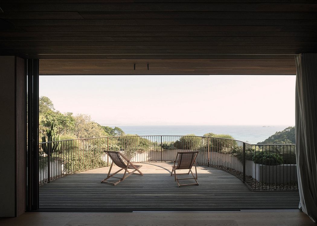 Expansive wooden deck with two lounge chairs overlooking lush greenery and ocean view.