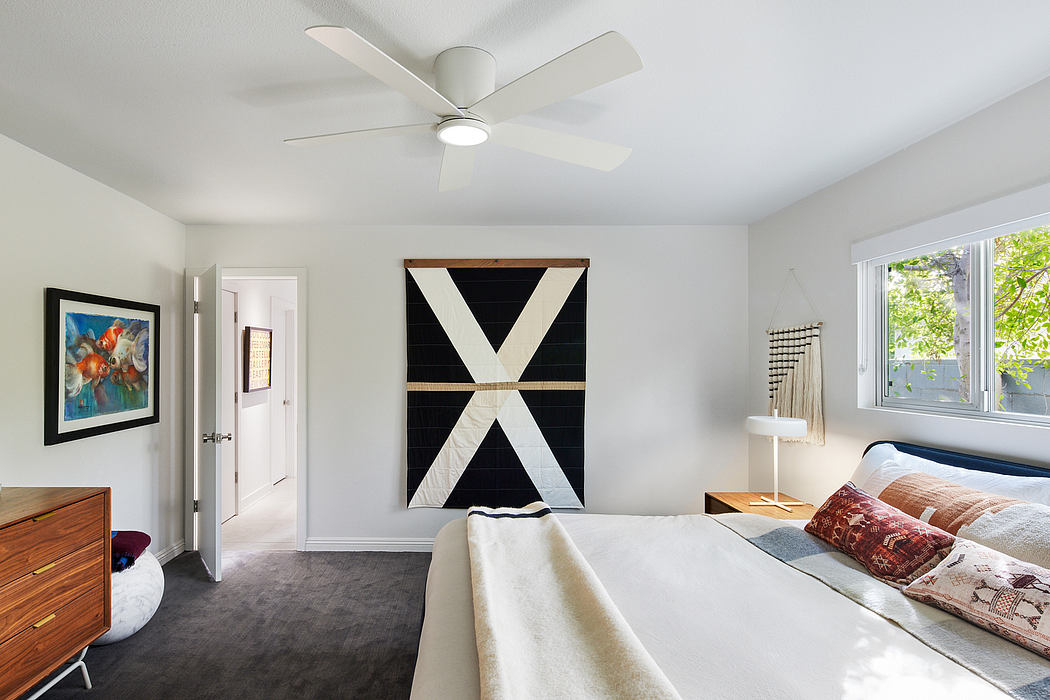 Minimalist bedroom with wooden furniture, geometric artwork, and ceiling fan.