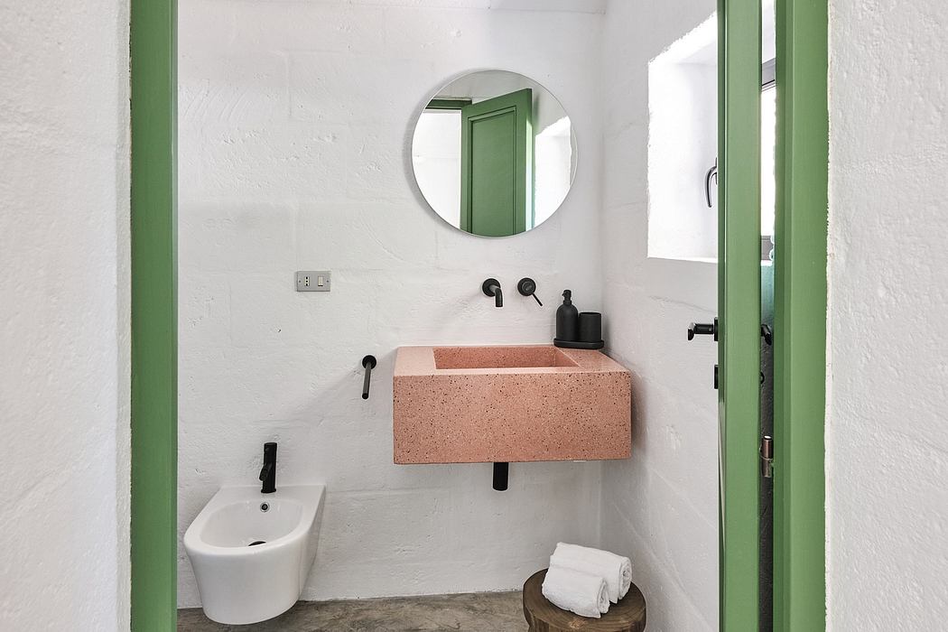A minimalist bathroom interior featuring a pink terrazzo sink, round mirror, and green accents.