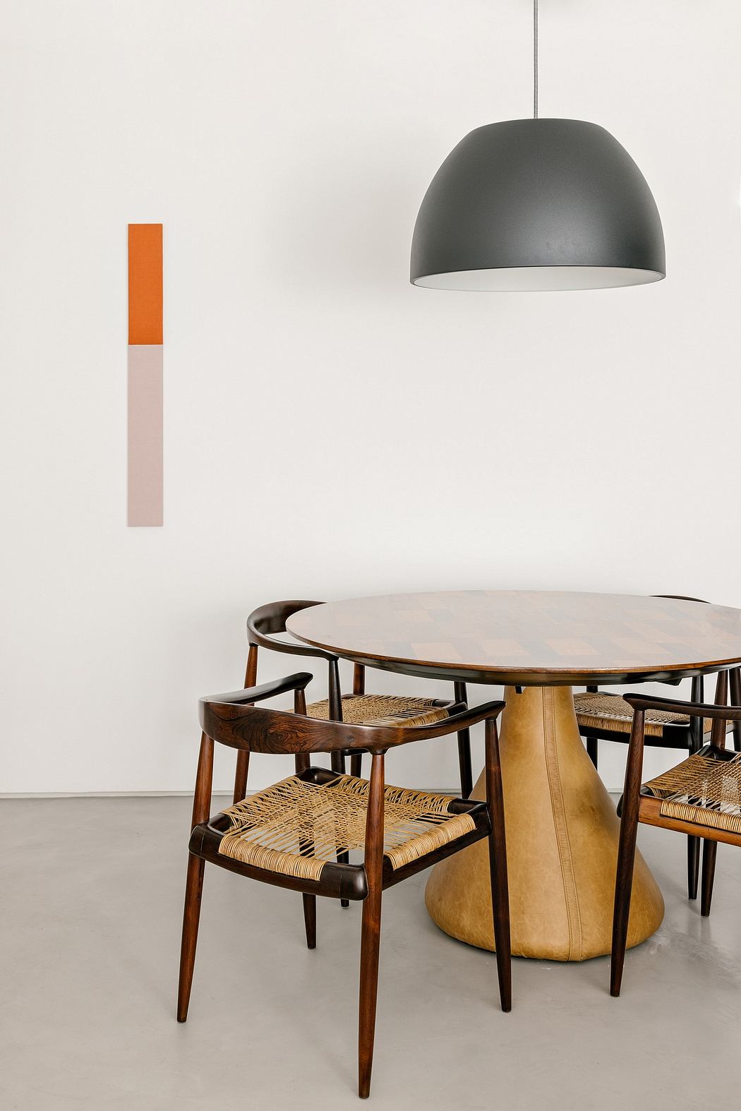 Sleek modern lighting fixture, round wooden pedestal table, woven seating.