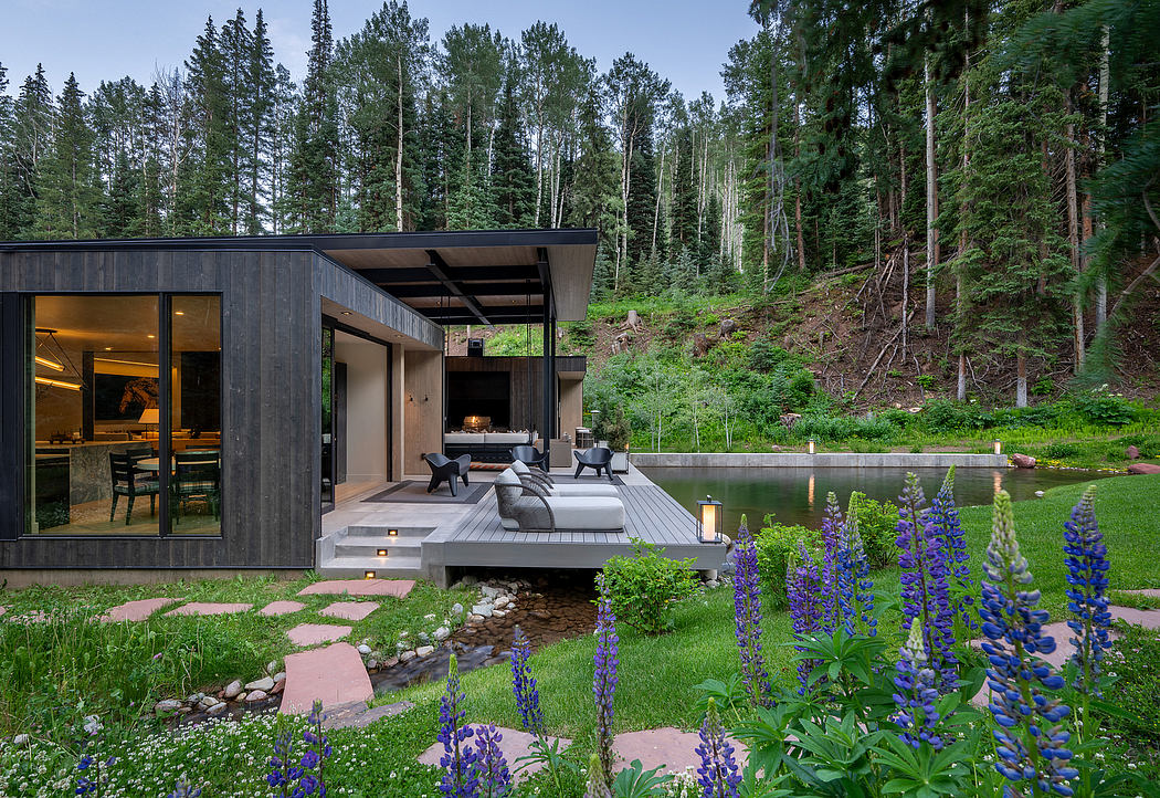A modern cabin with a spacious deck overlooking a lush forest landscape and a pond.