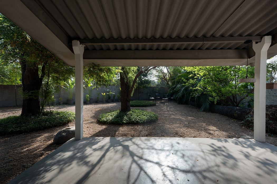 Covered patio with ornate roof beams, surrounded by lush greenery and a gravel path.