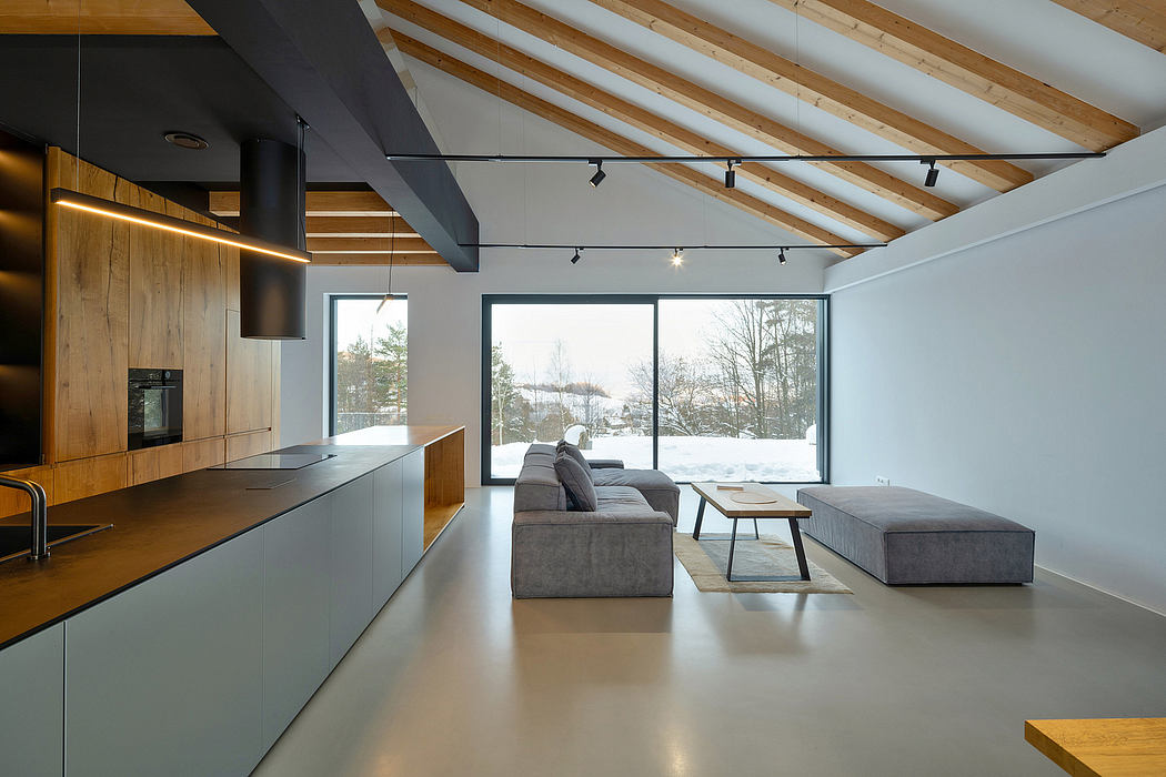 A modern, open-concept living space with wooden beams, large windows, and gray furniture.