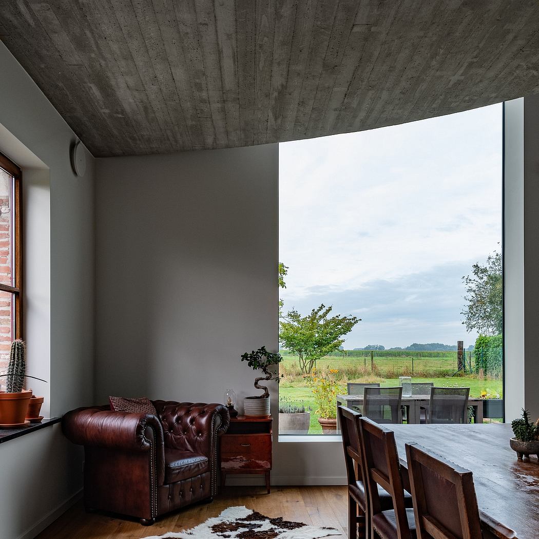 Rustic concrete ceiling, chesterfield sofa, expansive window framing nature view.