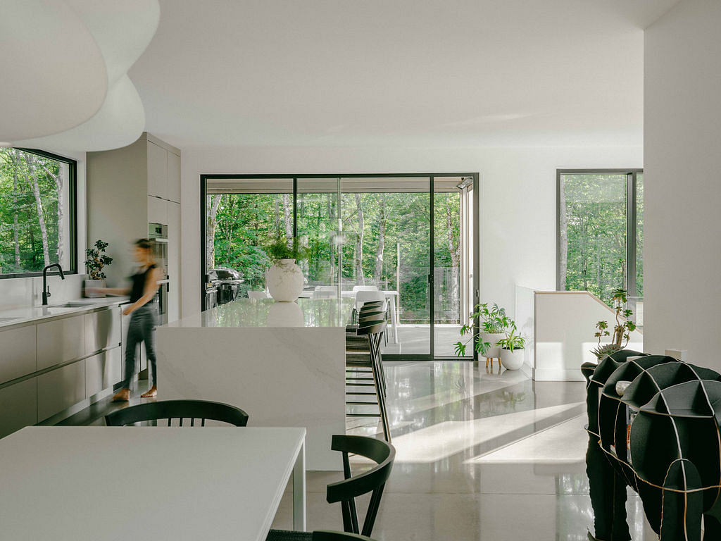 Bright, modern kitchen and dining area with expansive glass walls overlooking nature.