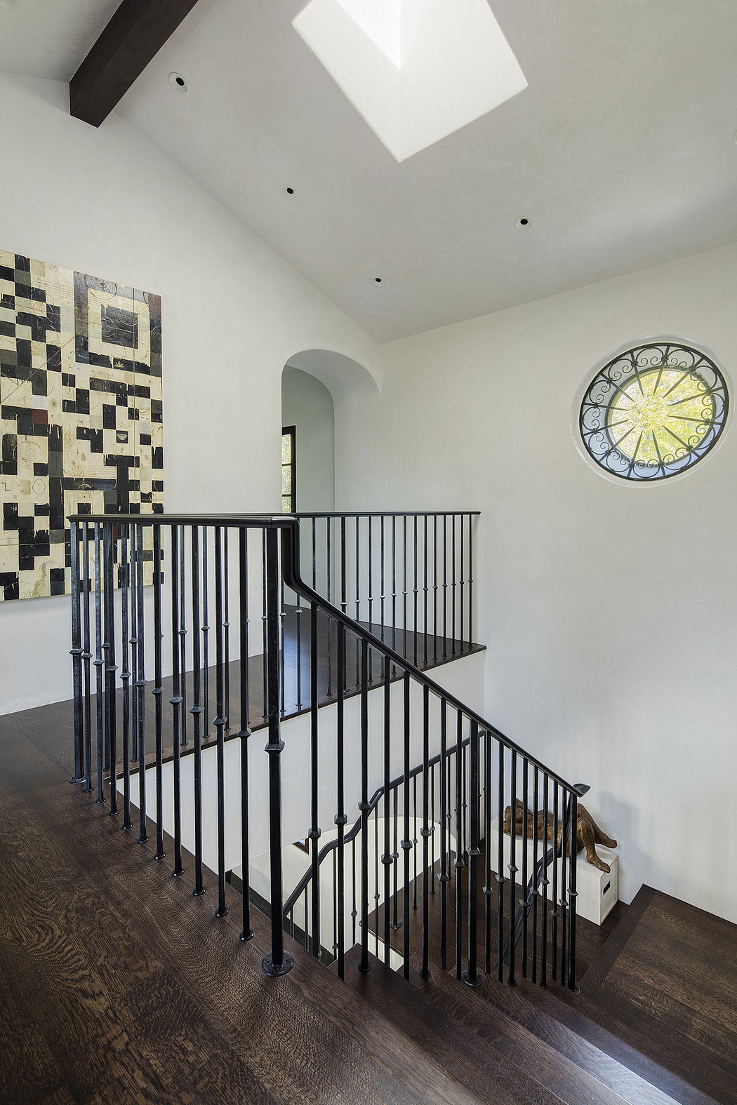 Ornate wrought-iron staircase with arched windows and modern artwork on walls.