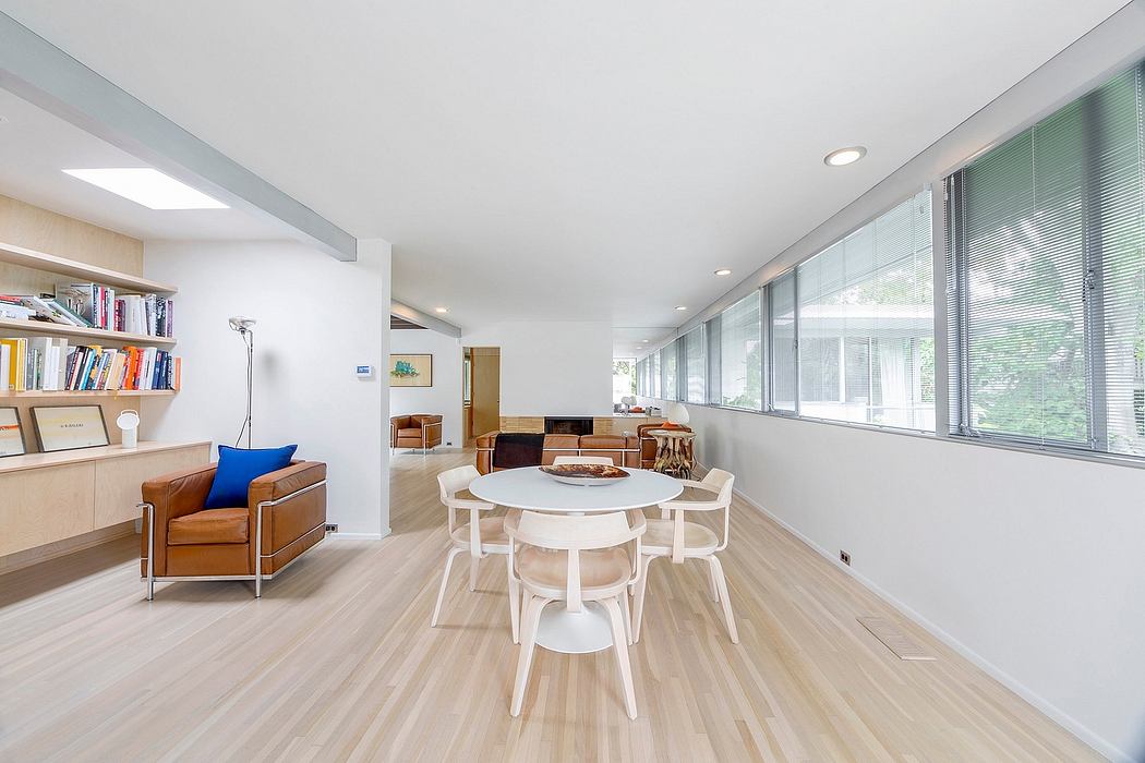 Spacious modern living room with large windows, white table and chairs, and bookshelves.