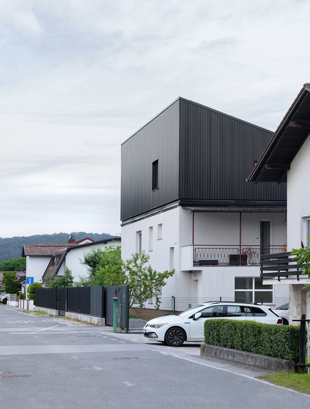 A modern gray building with a balcony and a parked white car in the foreground.