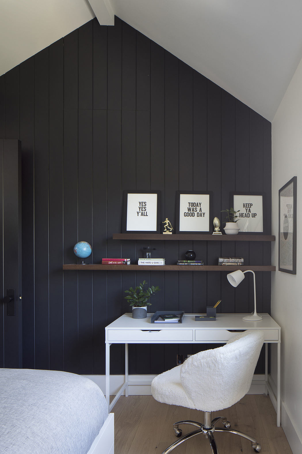 Warm, minimalist bedroom with black paneled walls, shelves, and white desk setup.