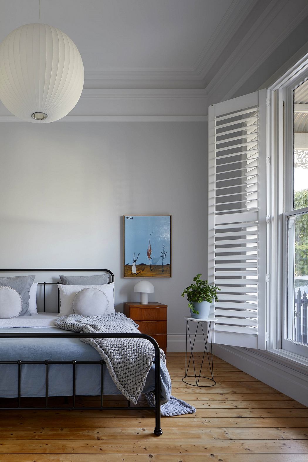 Cozy bedroom with sleek metal bed frame, pendant light, and wooden floors.