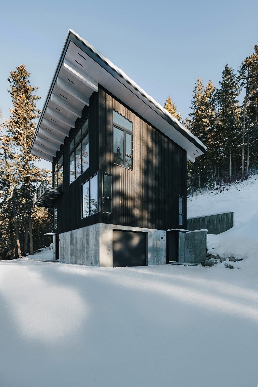 Striking modern cabin with angled roofline and expansive windows nestled in snowy forest.