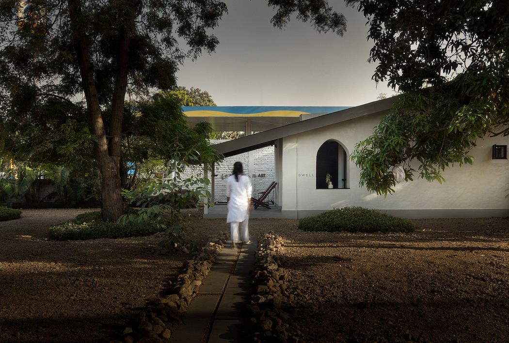 A white building with arched windows and a path leading to it, surrounded by lush greenery.