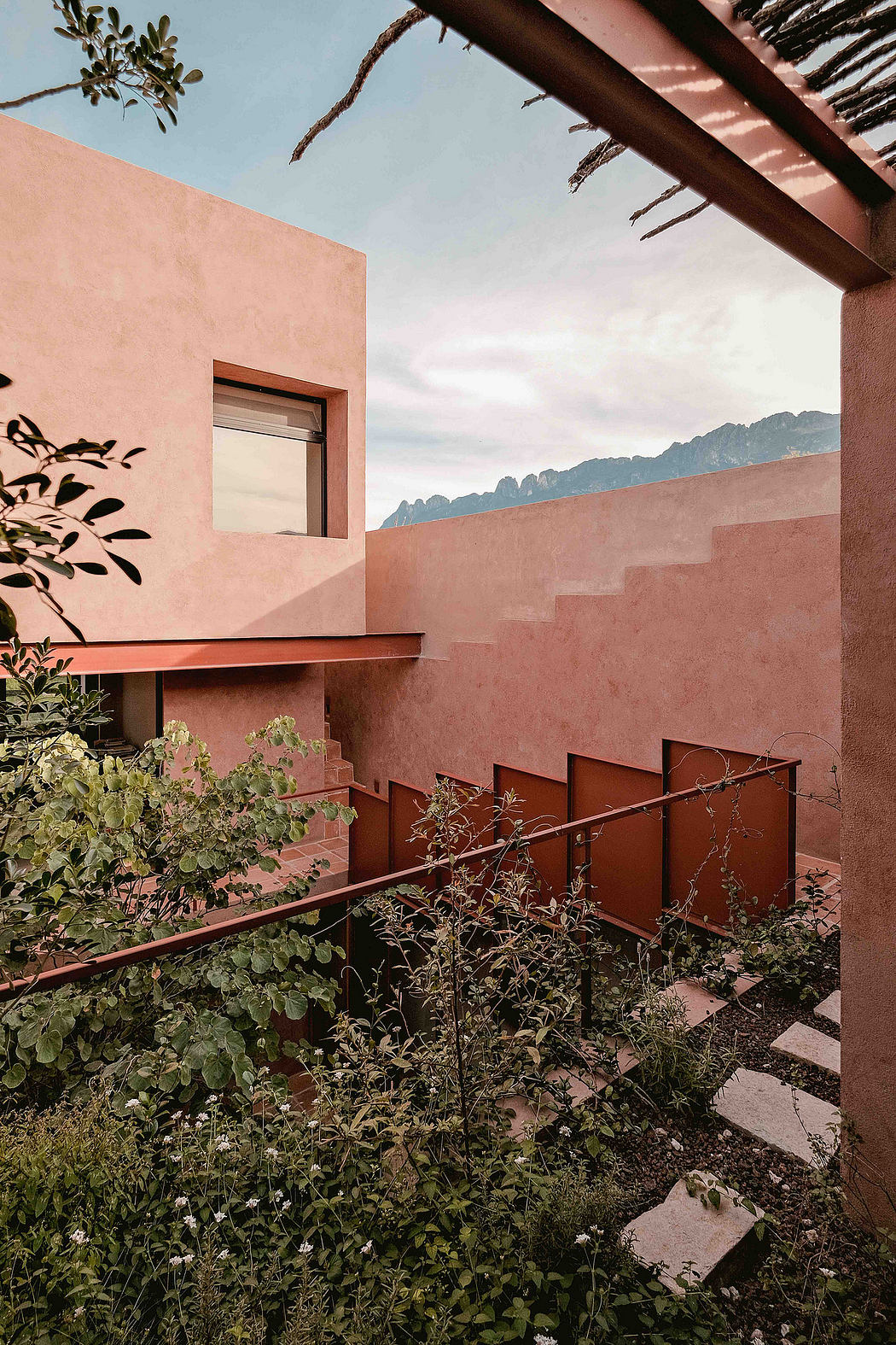 Minimalist architectural design features pink stucco walls, wooden beams, and lush greenery.