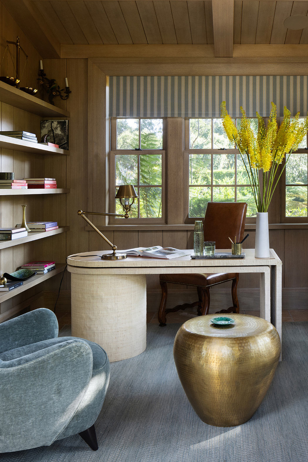 Cozy home office with warm wood paneling, built-in shelves, and a brass garden stool.