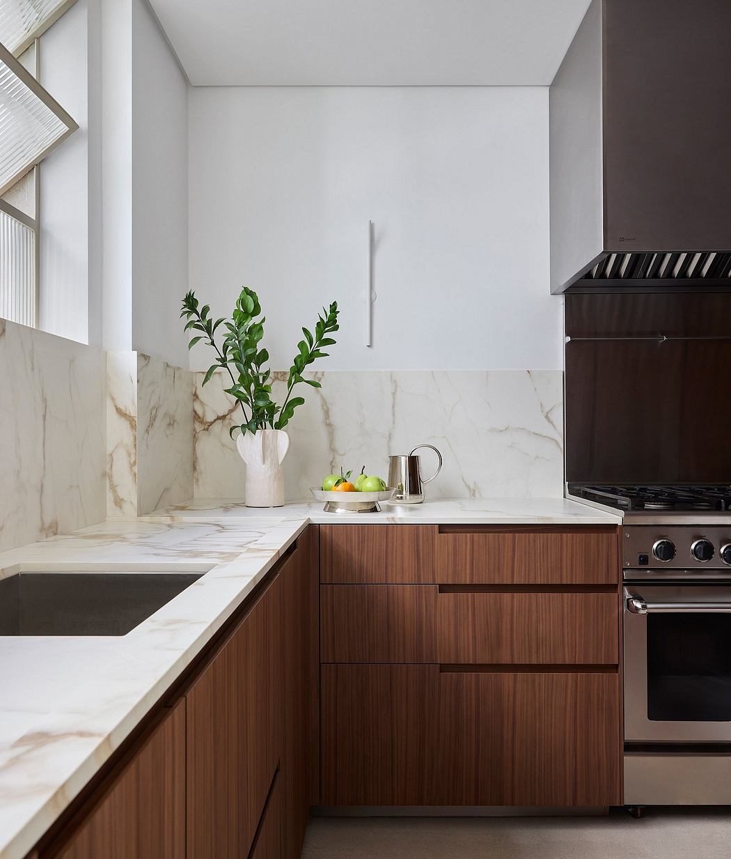 Sleek, modern kitchen with marble countertops, wood cabinets, and a potted plant.