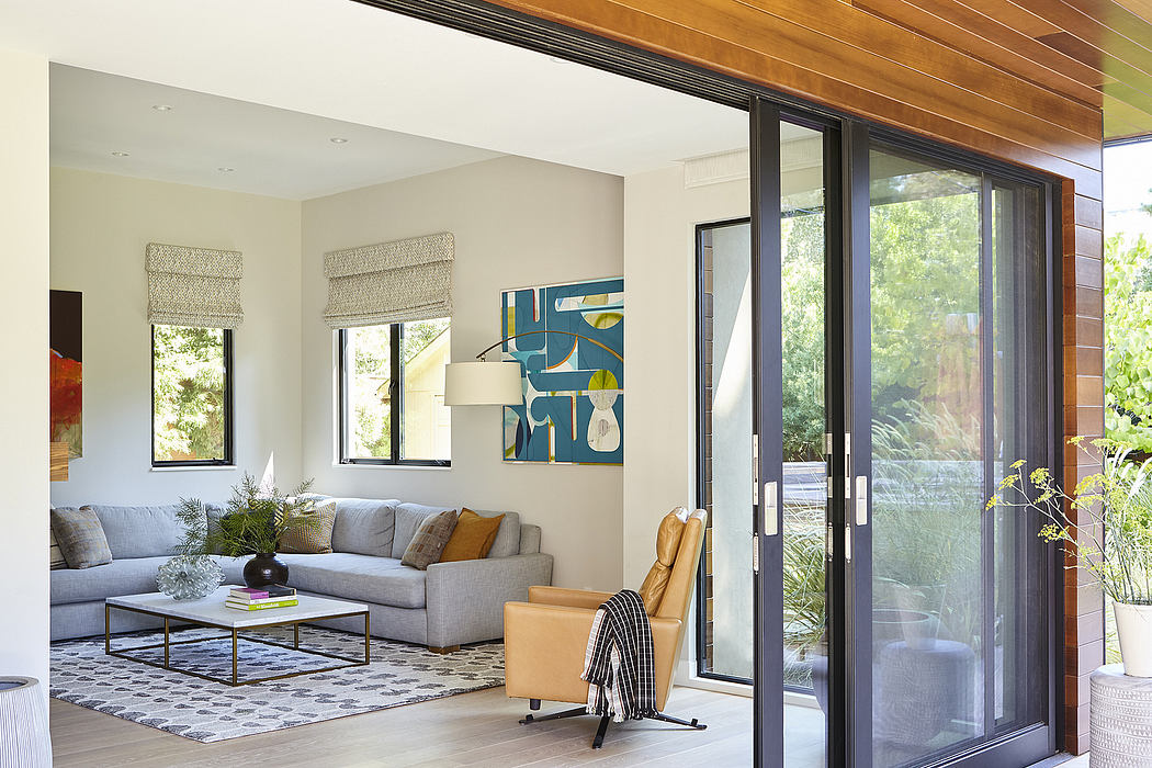 A bright, modern living room with large windows, a gray sectional, and an abstract artwork.