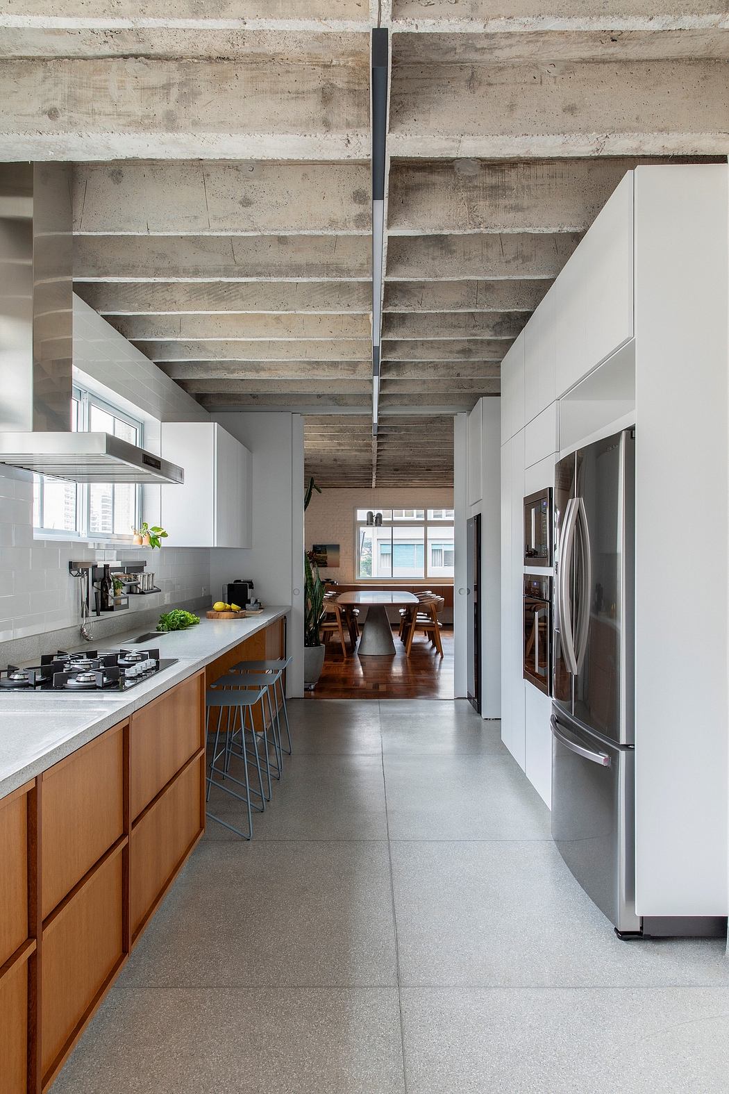 A modern kitchen with exposed concrete ceiling, wood cabinetry, and stainless steel appliances.