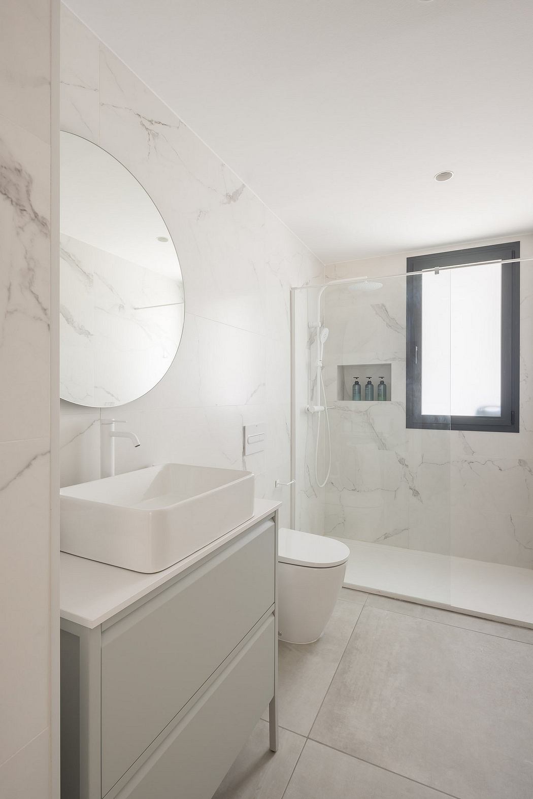 A bright, minimalist bathroom with sleek marble walls, a rectangular sink, and a glass shower.