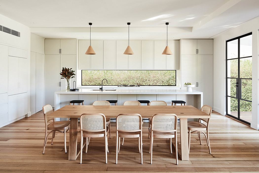Minimalist kitchen and dining area with large window, wooden furniture, and pendant lights.
