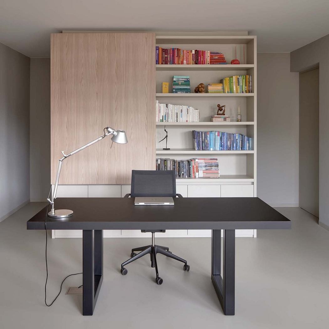 Minimalist home office with sleek black desk, adjustable lamp, and built-in shelving.