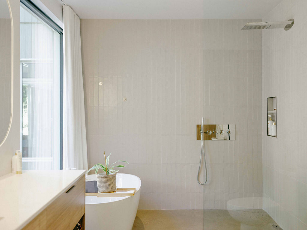 Spacious, minimalist bathroom with large window, wooden vanity, and recessed shelving.