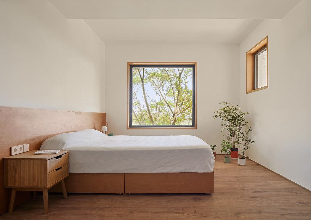 A modern bedroom with wooden furniture, large window, and potted plant, showcasing a minimalist design.