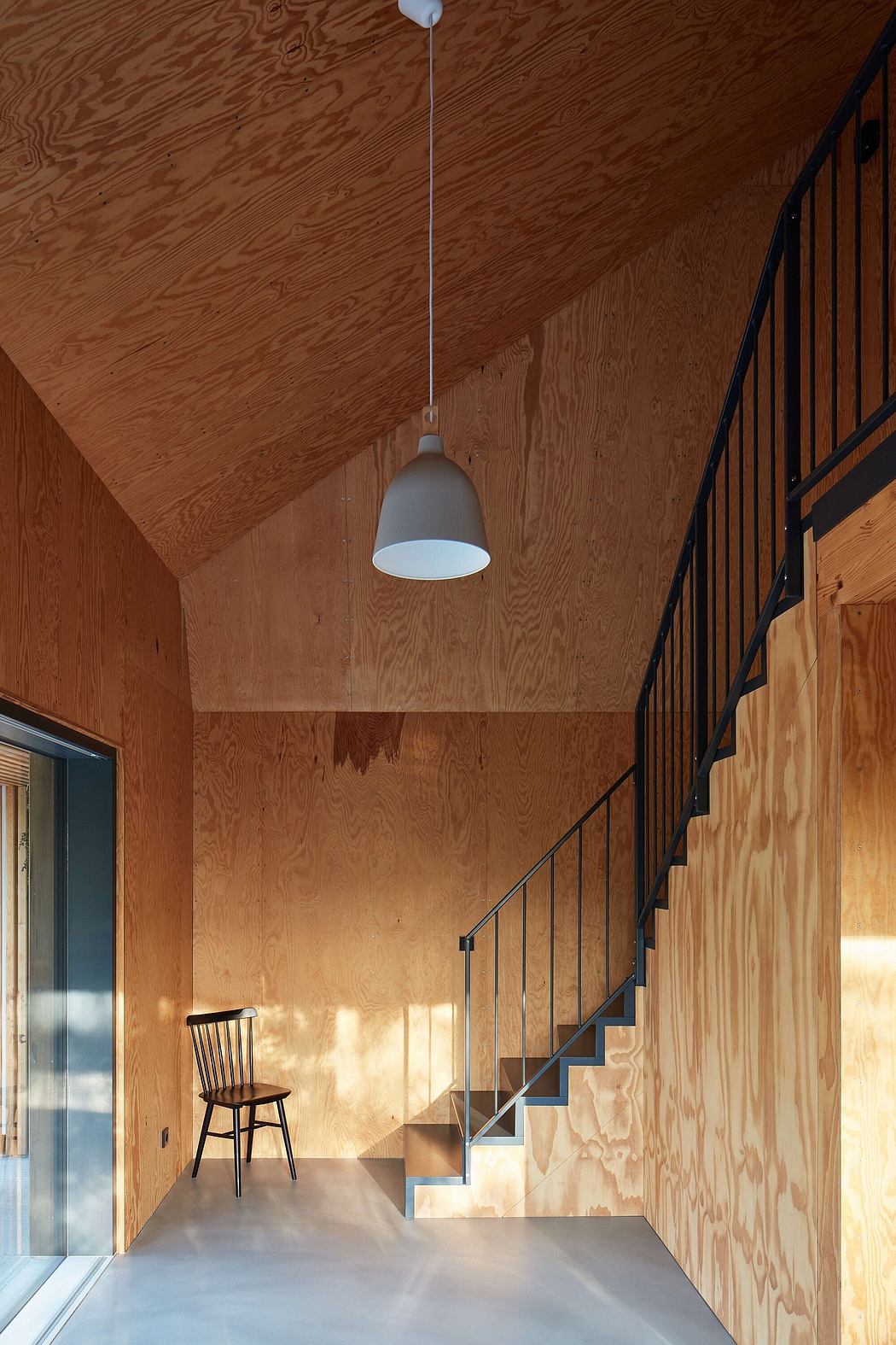 Warm-toned wooden walls, minimalist staircase, and hanging light fixture in a modern interior.