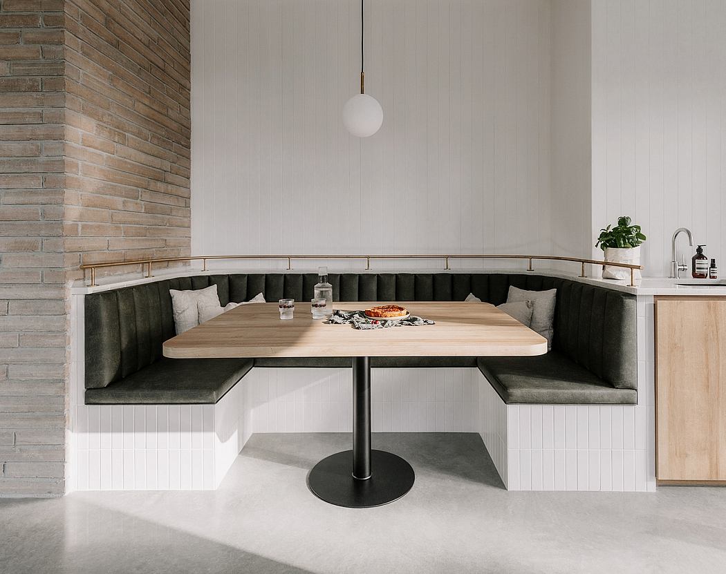 Modern kitchen dining nook with curved upholstered bench, wood table, and pendant light.