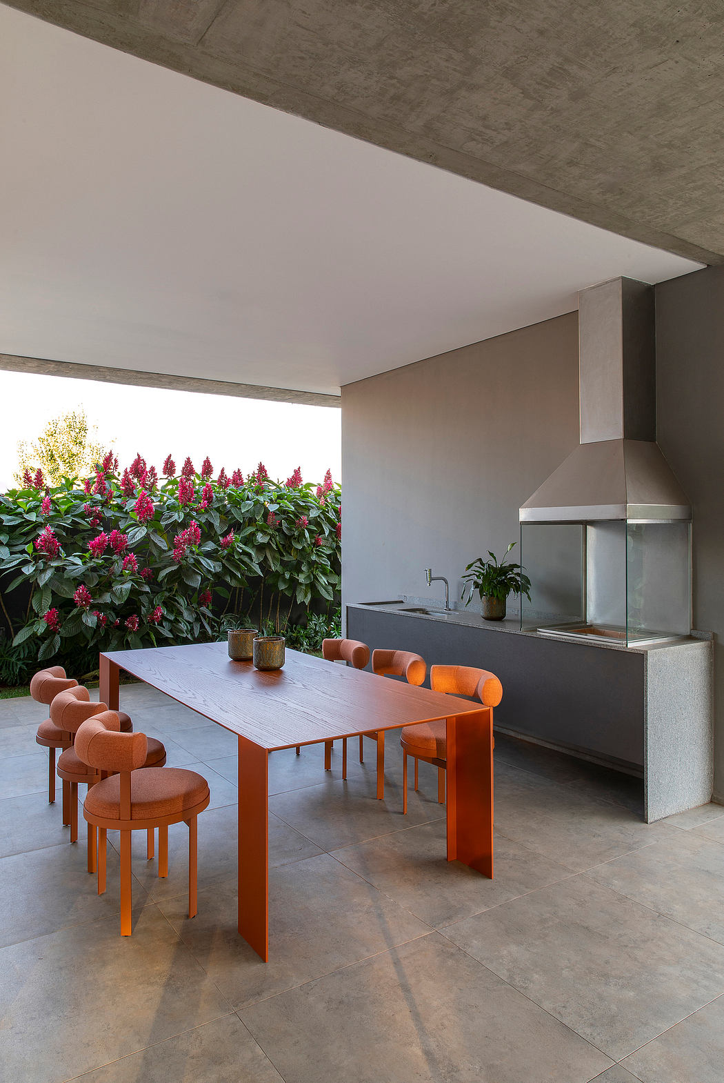 Minimalist indoor-outdoor dining area with concrete ceiling, sleek kitchen, and vibrant flowers.