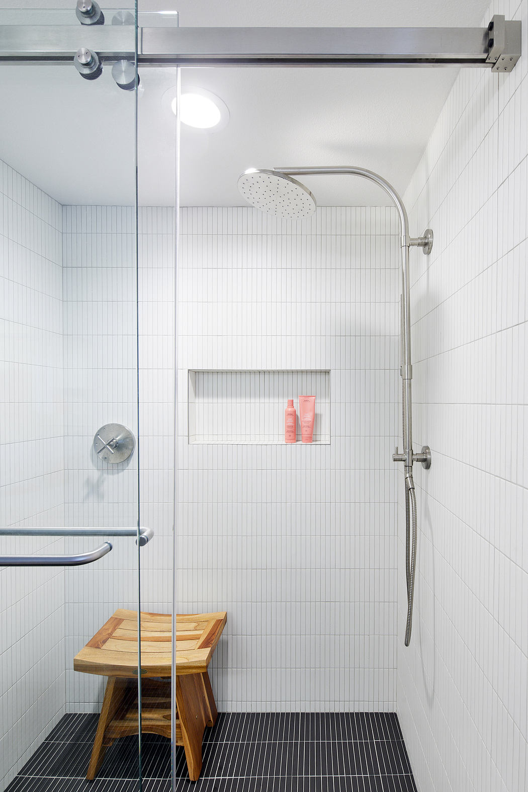Modern bathroom with minimalist design, glass shower enclosure, and wooden bench.