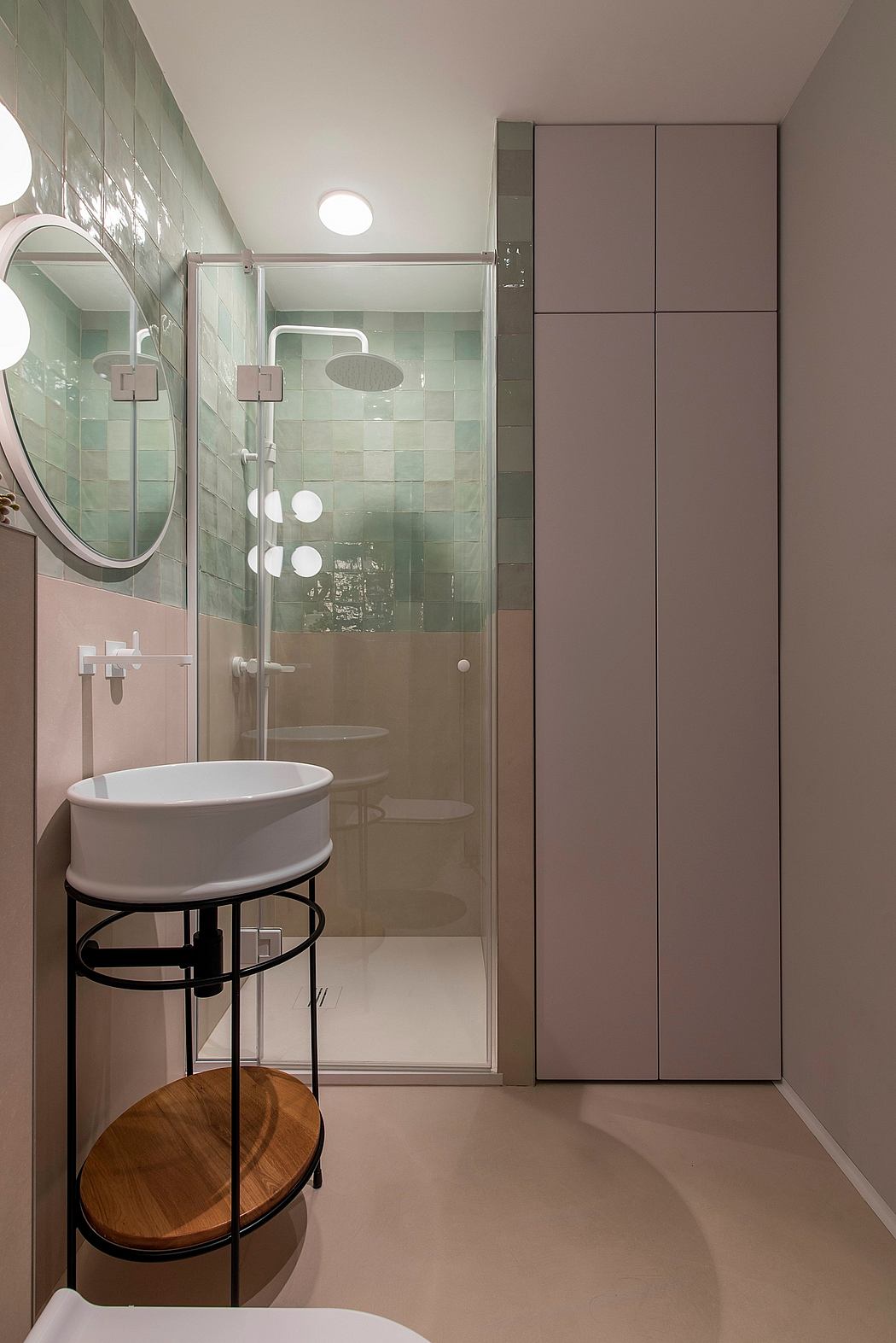 A modern bathroom with mint green tiles, a circular mirror, and built-in storage cabinets.