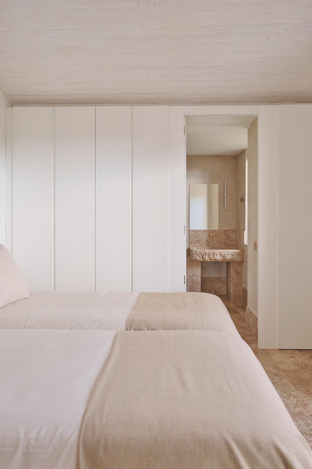 A minimalist bedroom with built-in closets, a stone vanity, and a neutral color palette.