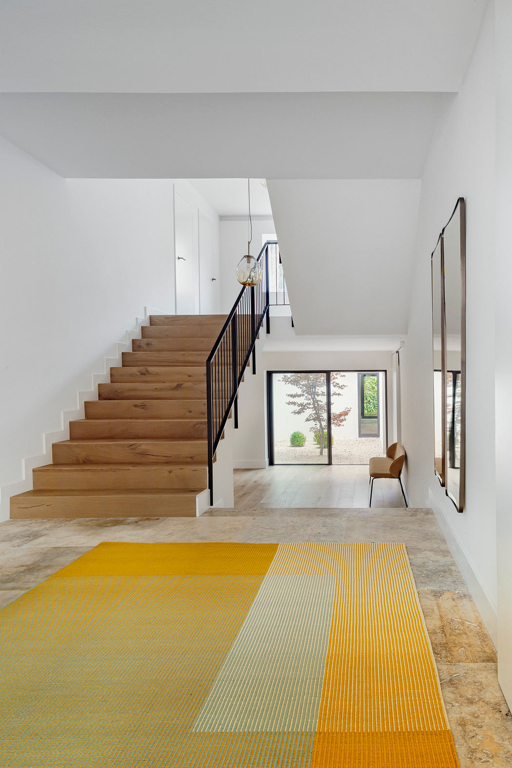 Elegant wooden stairs, sleek metal railing, and vibrant yellow rug in modern foyer.
