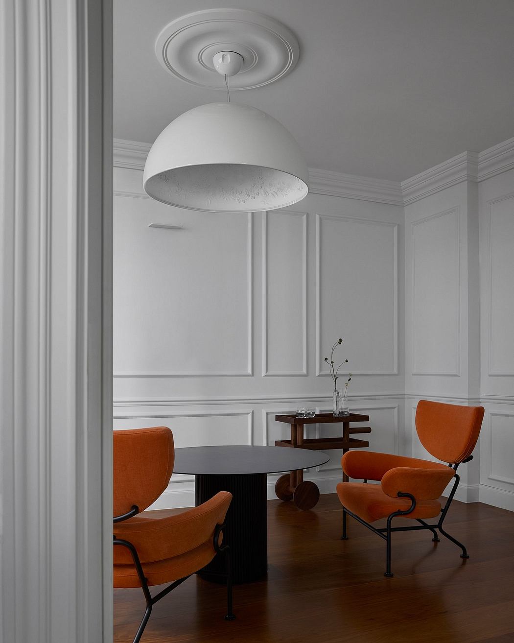 Minimalist modern dining room with sleek white dome light fixture and warm orange chairs.