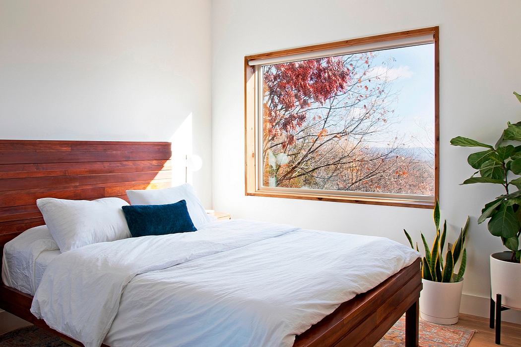A cozy bedroom with a wooden bed frame and a large window overlooking fall foliage.