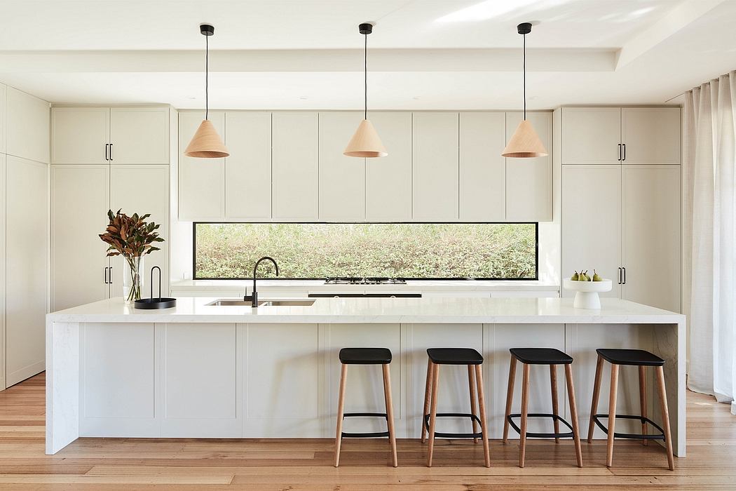 Modern, minimalist kitchen with sleek white cabinetry, pendant lighting, and a panoramic window overlooking greenery.