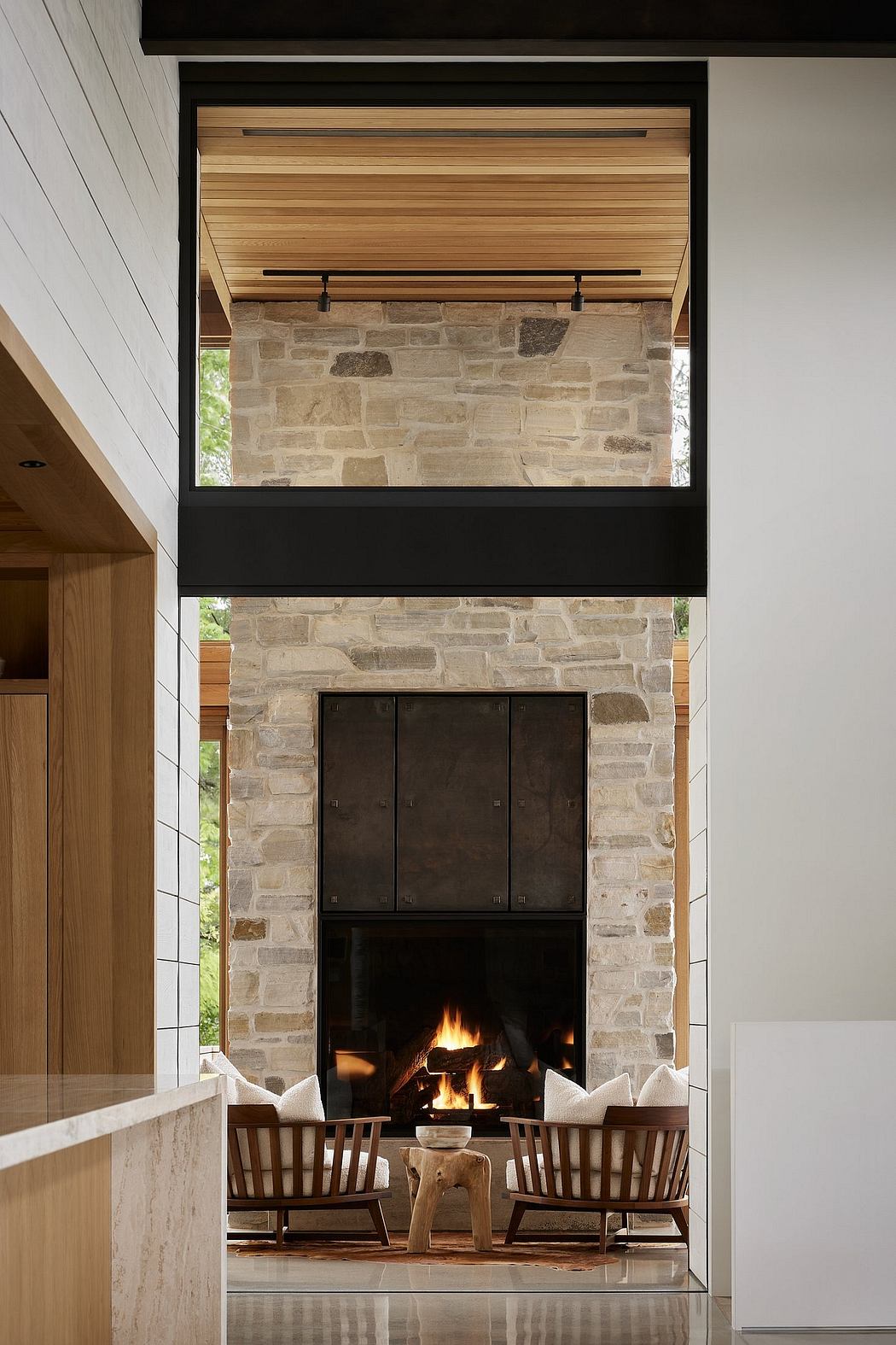 Stone fireplace with wooden beams, chairs, and a wooden stool in a cozy interior.