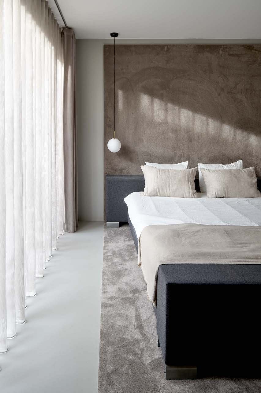A minimalist bedroom with a concrete wall, white bedding, and a pendant light fixture.