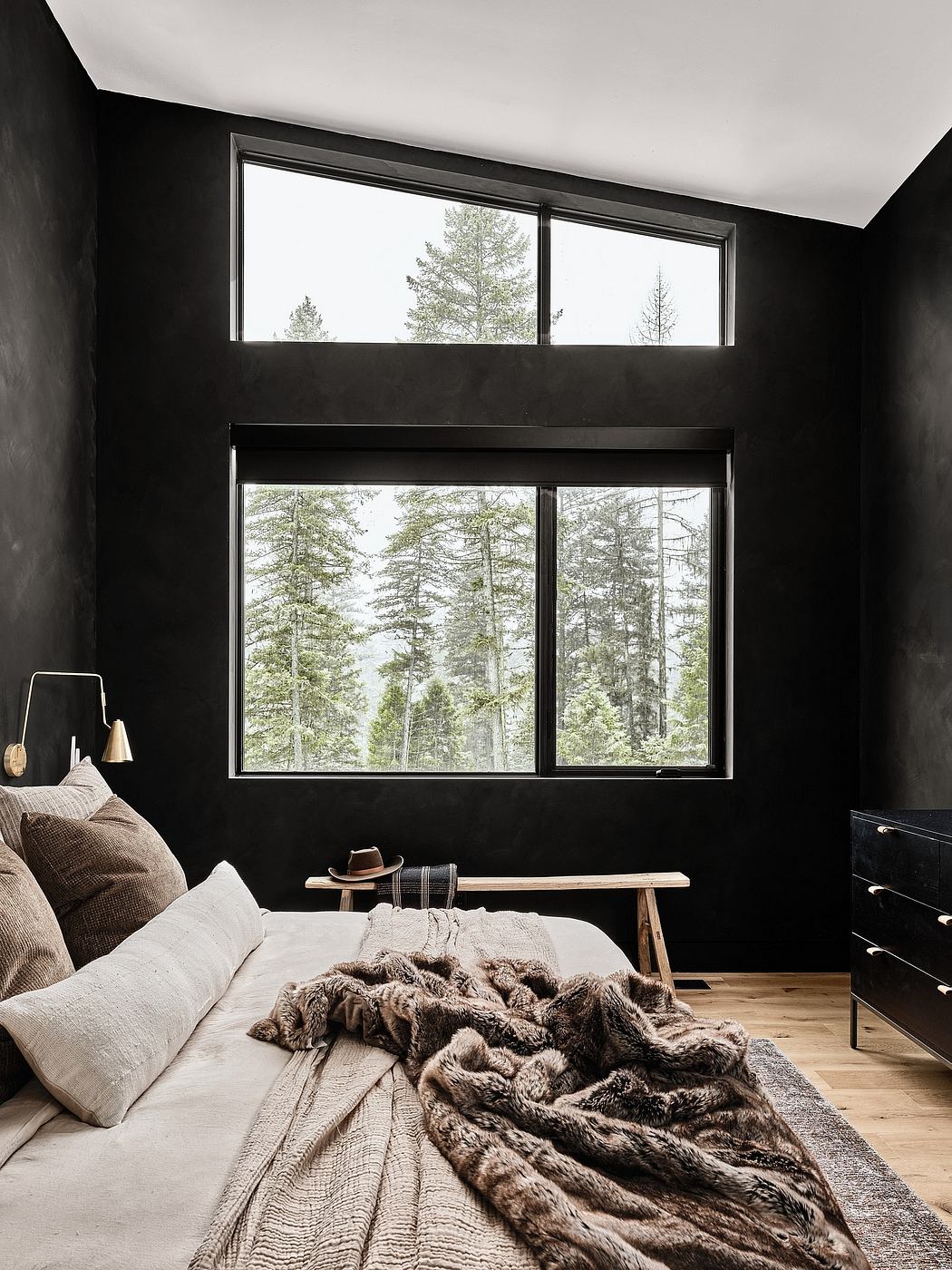 Cozy cabin bedroom with large windows overlooking a lush forest landscape.