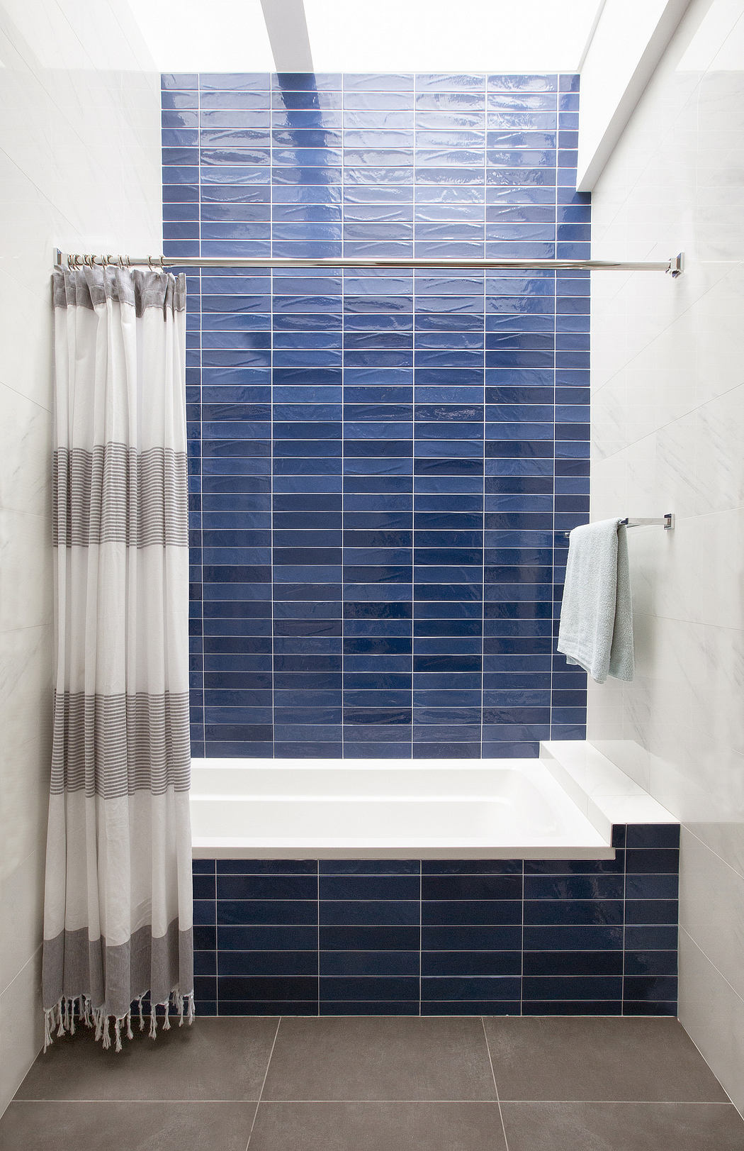 A modern bathroom with a striking blue tiled wall and clean white fixtures.
