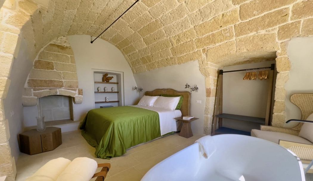 A cozy bedroom with rustic stone walls, wood furnishings, and a charming fireplace.