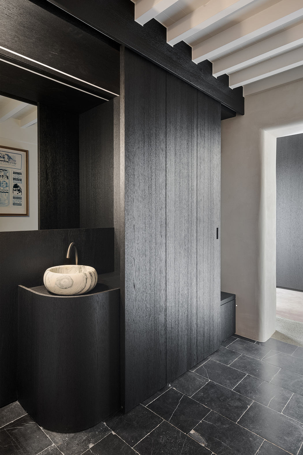 Sleek, modern bathroom with black wood paneling, unique stone sink, and slate tile flooring.