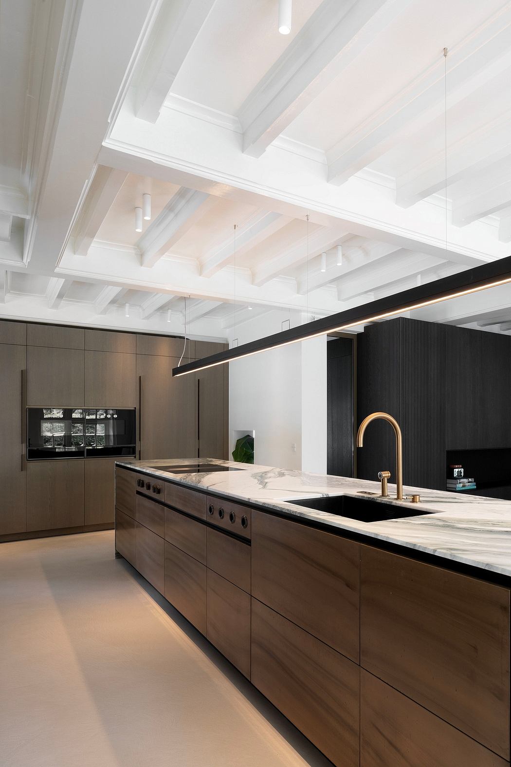 A modern kitchen with sleek cabinetry, marble countertops, and a linear pendant lighting design.