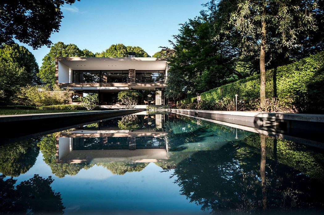 A modern, open-concept house with a reflection pool and lush, forested surroundings.