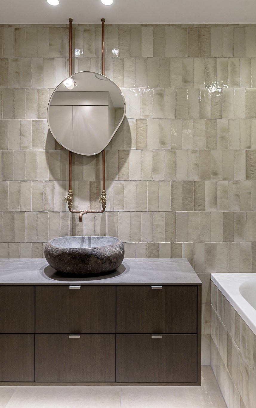 A modern bathroom with a round mirror, stone vessel sink, and sleek wooden cabinetry.