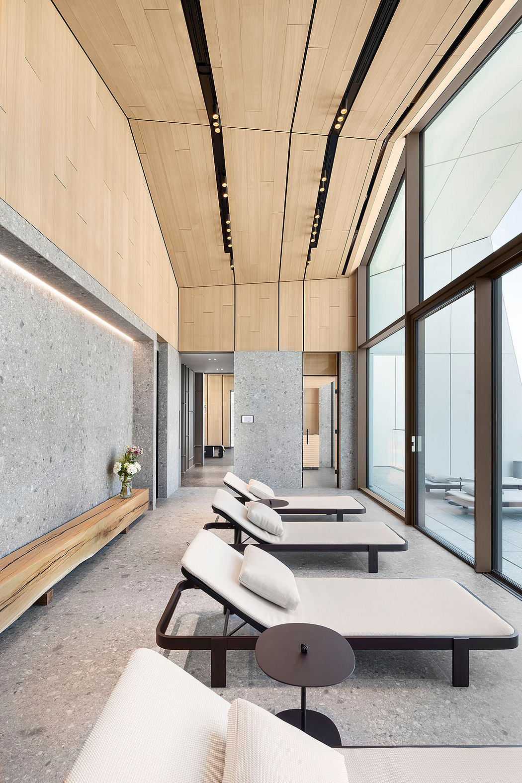 Modern interior with wooden paneled ceiling, gray stone walls, and sleek lounge chairs.