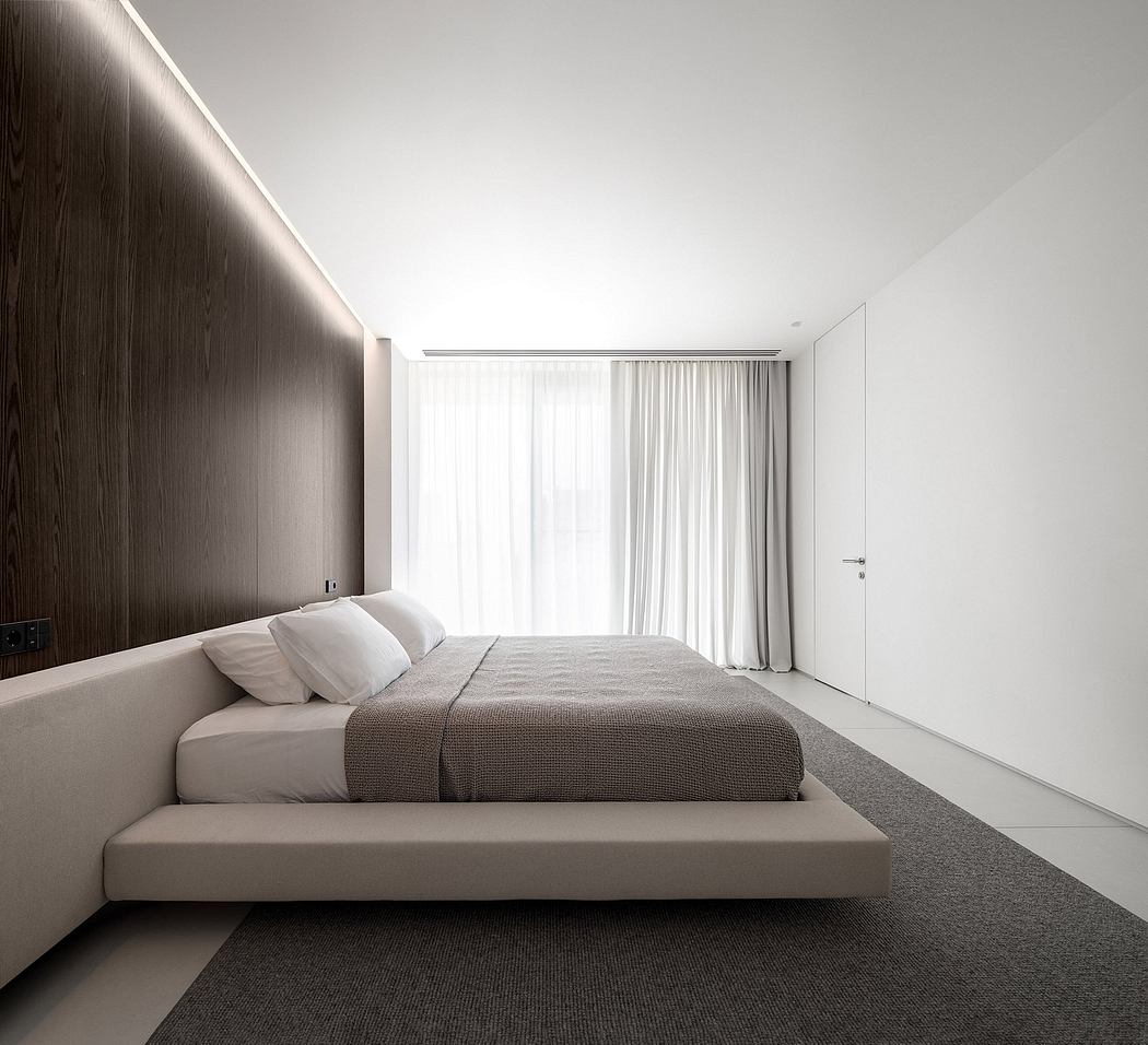 Minimalist bedroom with dark wood accent wall, white curtains, and large gray bed.